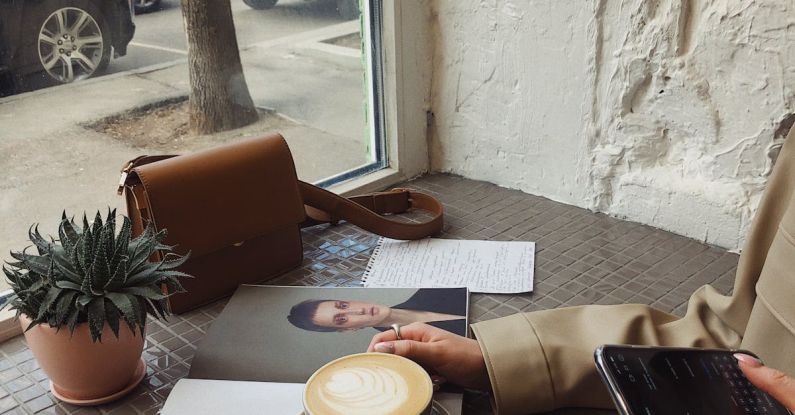 Enjoyable Trips - Crop of unrecognizable female tourist in casual wear surfing internet and flipping magazine while drinking coffee in sidewalk cafe