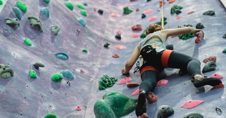 Hike Training - From below of anonymous female equipped with safety rope and harness moving up at rock climbing wall at gym