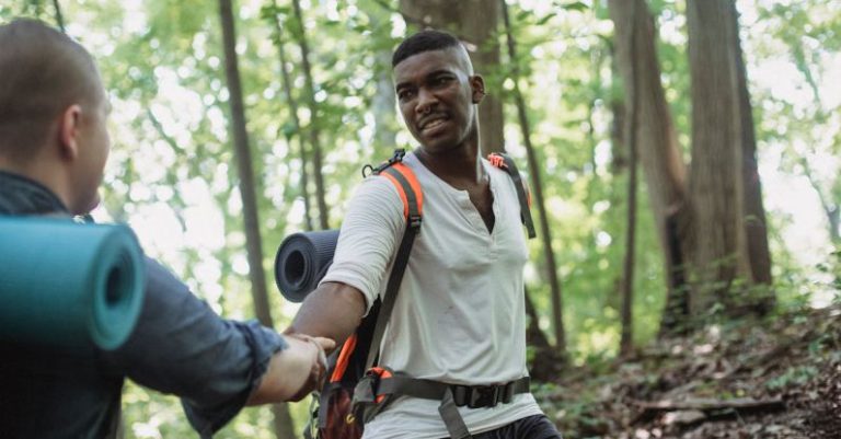 Hiking Uphill - African American hiker helping man to climb up