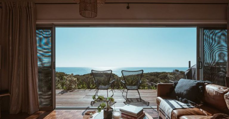 Luxury Accommodations - Interior design of luxurious apartment with large balcony doors and wooden terrace having picturesque view on green forested seashore and calm blue sea