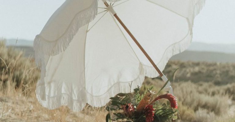 Day Trips - Small wicker basket with fresh wildflowers under white umbrella left on sandy beach in sunny day